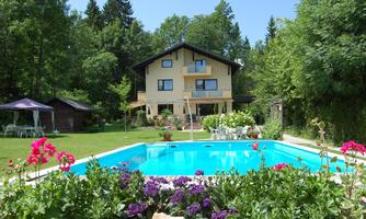 A beautiful house with a pool, surrounded by colorful flowers and lots of greenery. The sun is shining and creates a relaxed holiday atmosphere.