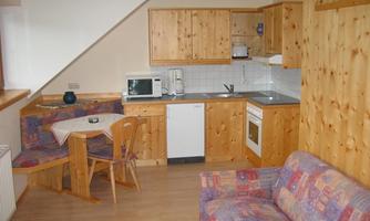 A cozy kitchen with wooden cabinets and a small dining area. There is a sofa in the room, and modern kitchen appliances are available.