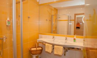 A modern bathroom with yellow walls and a spacious sink. On the wall, showers and a mirror can be seen.