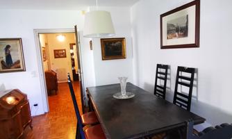 An elegant dining area with a dark table and wooden chairs. Artwork hangs on the walls, and a light is hanging from the ceiling.