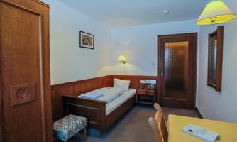 A simple room with a bed, a bench, and a table. The walls are light and there is a pleasant lighting.