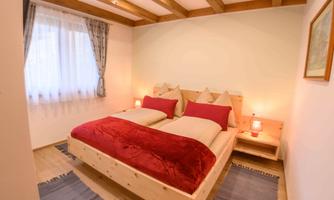 A cozy bedroom with a double bed and red pillows. There are wooden ceiling beams and a bright atmosphere.
