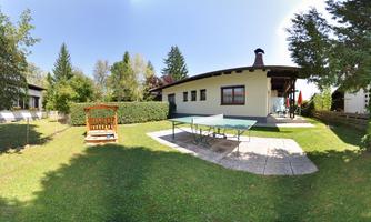 A cozy house with a large garden, surrounded by trees. In the garden, there is a swing and a table tennis table.