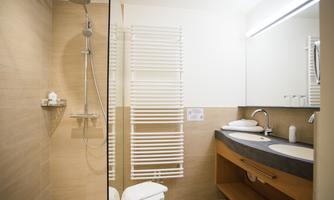 A modern bathroom with a shower and two sinks. The walls are in warm tones, and there is plenty of natural light.