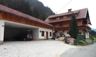 A cozy house in Alpine style with a large garage area. Surrounded by nature and mountains, it conveys a rustic charm.