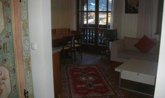 A cozy living room with a table, chairs, and a couch. The room has a carpet and large windows overlooking the mountains.