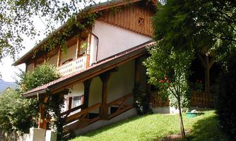 A charming country-style house surrounded by green countryside. The balcony and wood paneling give it an inviting character.