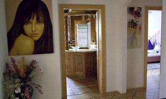 An inviting hallway with a large painting of a woman and a beautiful flower arrangement. In the background, an open kitchen with wooden details can be seen.