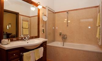 A modern bathroom with a bathtub and a shower. The walls are light, and there are wooden elements as well as soft towels.
