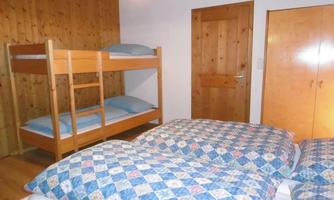 A cozy bedroom with a double bed and a bunk bed. The walls are made of wood, and there is warm lighting.