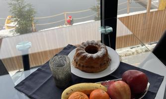 A beautiful table with fresh fruit and a cake. In the background, there is a window with a view of the water.