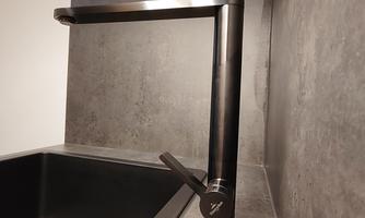 A modern black kitchen faucet above a black sink. The wall is made of gray material, creating an elegant look.