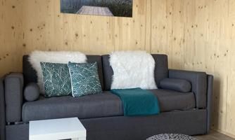 A cozy living room with a gray sofa and colorful cushions. Next to the sofa is a small white table and a round pouf on a rug.