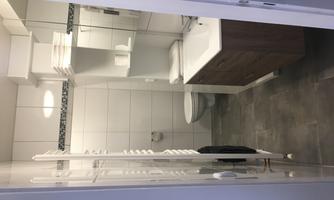 A modern bathroom with white tiles and a large mirror. There are wooden under-sink cabinets and a towel radiator.