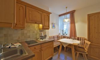 A cozy kitchen with wooden cabinets and a dining area. The table is set for a meal and there is plenty of daylight.