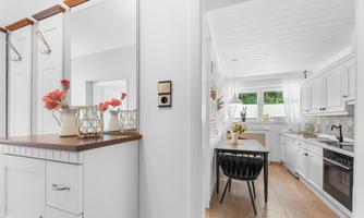 A bright entrance area with modern furnishings and white walls. In the background, an open kitchen with a cozy dining area can be seen.