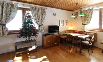 A cozy room with a small Christmas tree and a dining area. Large windows let in plenty of light and the wooden paneling creates a warm atmosphere.