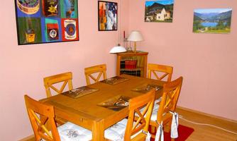 A cozy dining area with a wooden table and six chairs. Colorful pictures hang on the walls, and the room features warm, inviting colors.