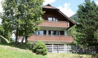 A charming wooden house surrounded by green meadows and trees. The clear sky creates an idyllic atmosphere.