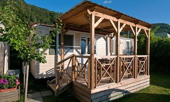 A cozy wooden house with a covered terrace. The surroundings are green and well-maintained, ideal for relaxation outdoors.