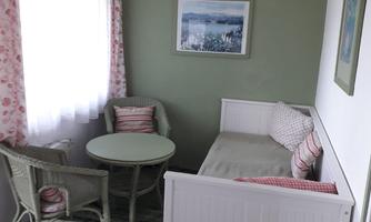 A cozy living area with a round table and two chairs. The walls are painted green, and there are light curtains and a beautiful picture.