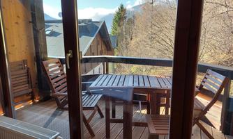 A cozy balcony with wooden furniture and a view of the surrounding mountains. The sun rays shine through the window, creating an inviting atmosphere.