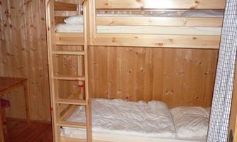 A cozy room with a wooden bunk bed. The walls are made of light wood and there is a simple decor.