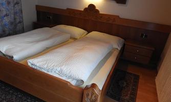 A cozy bedroom with a wooden bed and two separate comforters. The walls are in neutral tones, and a rug complements the room.