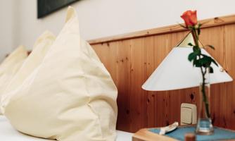 A cozy room with beige cushions and a nightstand. On the table, there is a lamp and a rose in a vase.