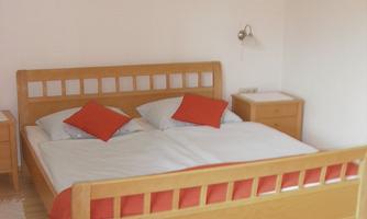 A cozy bedroom with a large wooden bed and red pillows. The walls are bright and the floor is covered with a rug.