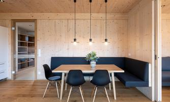 A modern dining room with a wooden table and black chairs. The walls are made of wood and there is a cozy bench with a flower vase on the table.