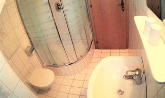 A modern bathroom with a shower cabin and a bathtub. The walls are tiled and there is a wooden door.