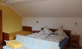 A cozy bedroom with two beds and a yellow wall. The bedding is colorful with a floral pattern.