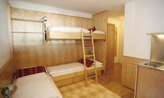 A simple room with a bunk bed and two single beds. The walls are bright and the room design is modern and functional.