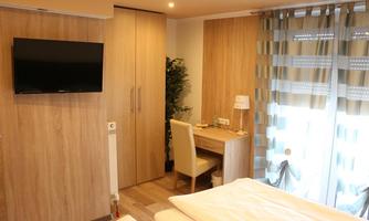 A cozy room with wooden walls and a television. There is a small desk and a view of the balcony.