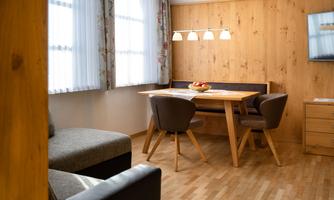 A modern living room with a wooden table and comfortable chairs. Large windows provide plenty of daylight and a cozy atmosphere.