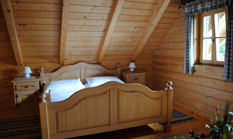 A cozy bedroom with wooden ceilings and a large bed. There are nightstands and a window that lets in light.