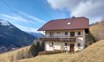 A detached house on a green meadow with a mountain in the background. The sky is partly cloudy.