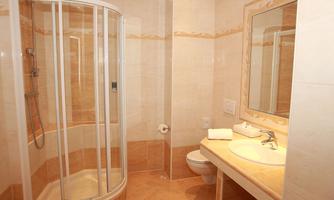 A modern bathroom with a shower cabin and a sink. The walls are tiled in light colors, and there is a large mirror.
