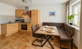 A modern kitchen with light wood cabinets and a dining area. Coffee and pastries are on the table.