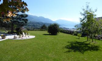 A spacious, green garden overlooking the mountains and the lake. The sun is shining and the sky is clear.