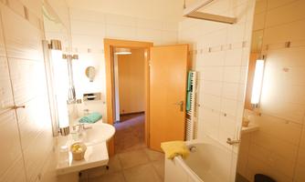 A modern bathroom with a bathtub and a sink. The walls are bright tiled and there is a door to an adjoining room.