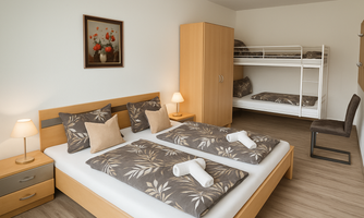A cozy bedroom with a double bed and a bunk bed. The decor is simple and modern with warm wood tones.