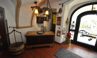 A cozy entrance area with a rustic wooden desk and two hanging lamps. The walls are adorned with traditional decorations and a large door leads outside.