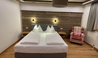 A cozy hotel room with a double bed and a comfortable armchair. The wooden paneling and soft lighting create an inviting atmosphere.