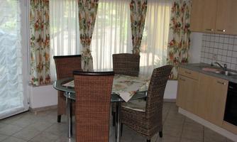 A cozy dining area with a round table and four rattan chairs. The windows are decorated with floral curtains that provide plenty of natural light.