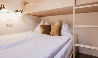 A cozy bedroom with a bunk bed and two single beds. The walls are light and the cushions are in soft tones.