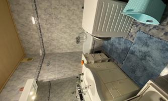 A small bathroom with a bathtub, a sink, and a washing machine. The walls are tiled with blue tiles and a blue carpet lies on the floor.