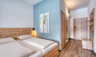 A modern bedroom with wooden beds and a simple design. The walls are painted in soft colors, and there is a window with natural light.