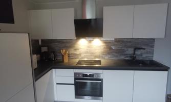 A modern kitchen with white cabinets and a wooden floor. The kitchen equipment includes a stove and a range hood.